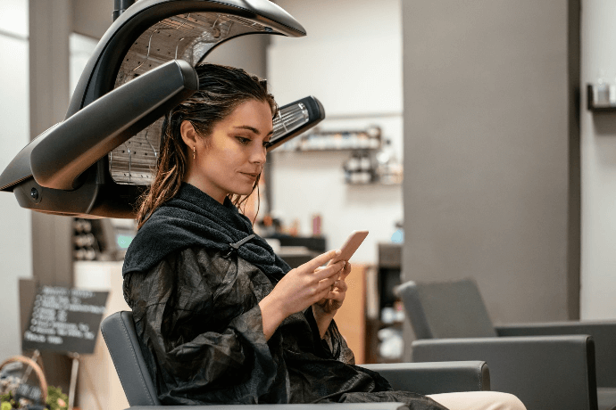 Cliente relajándose bajo secador de cabello en salón de belleza Cliente relajándose bajo secador de cabello en salón de belleza