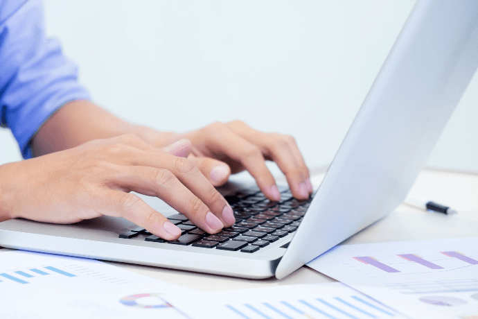 Manos escribiendo en portátil con gráficos y documentos legales Manos escribiendo en portátil con gráficos y documentos legales